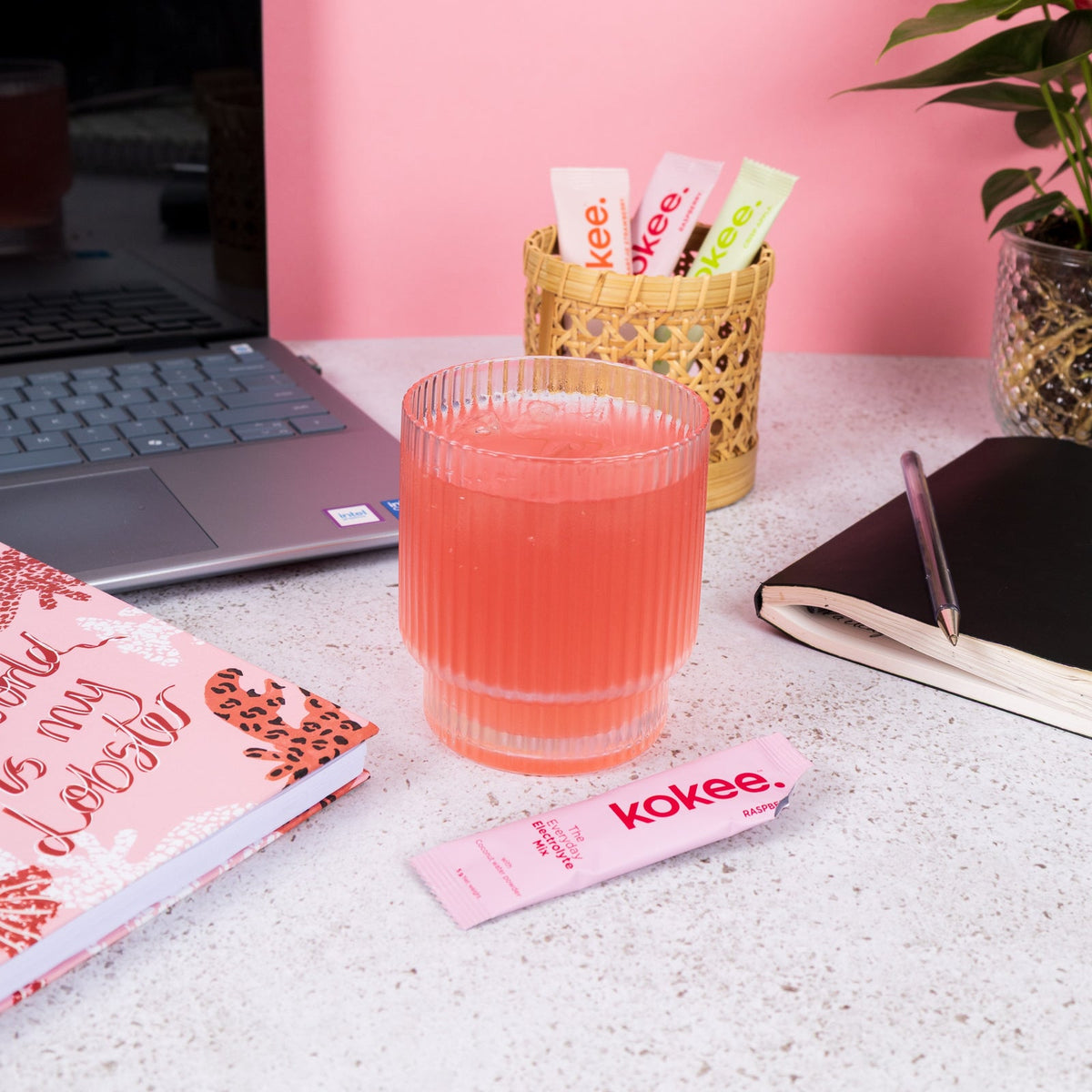 Pink Kokee drink on a desk next to a laptop and Kokee sachets